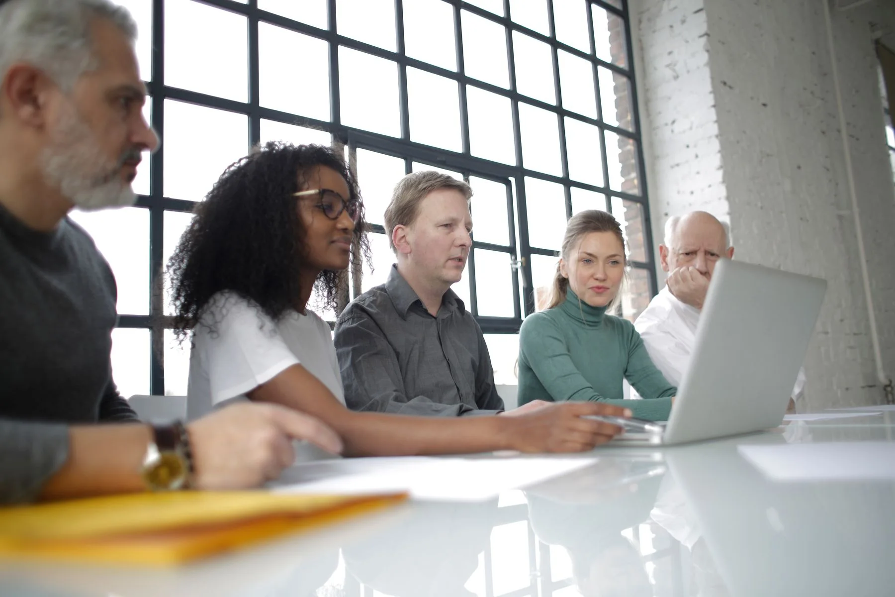 A diverse team collaborating around a laptop in a bright meeting room